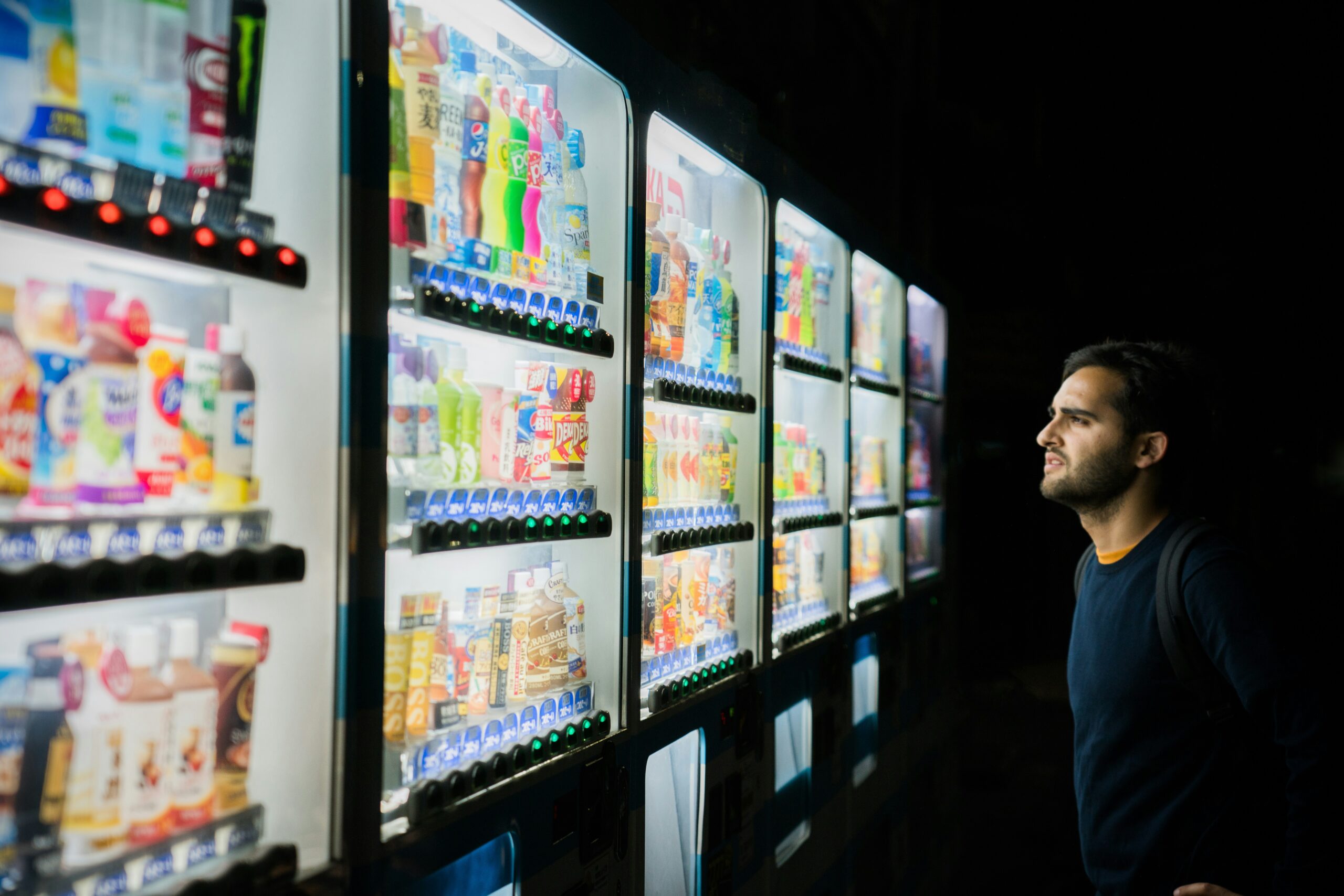 Image of a man standing at a wall of vending machines with many options.