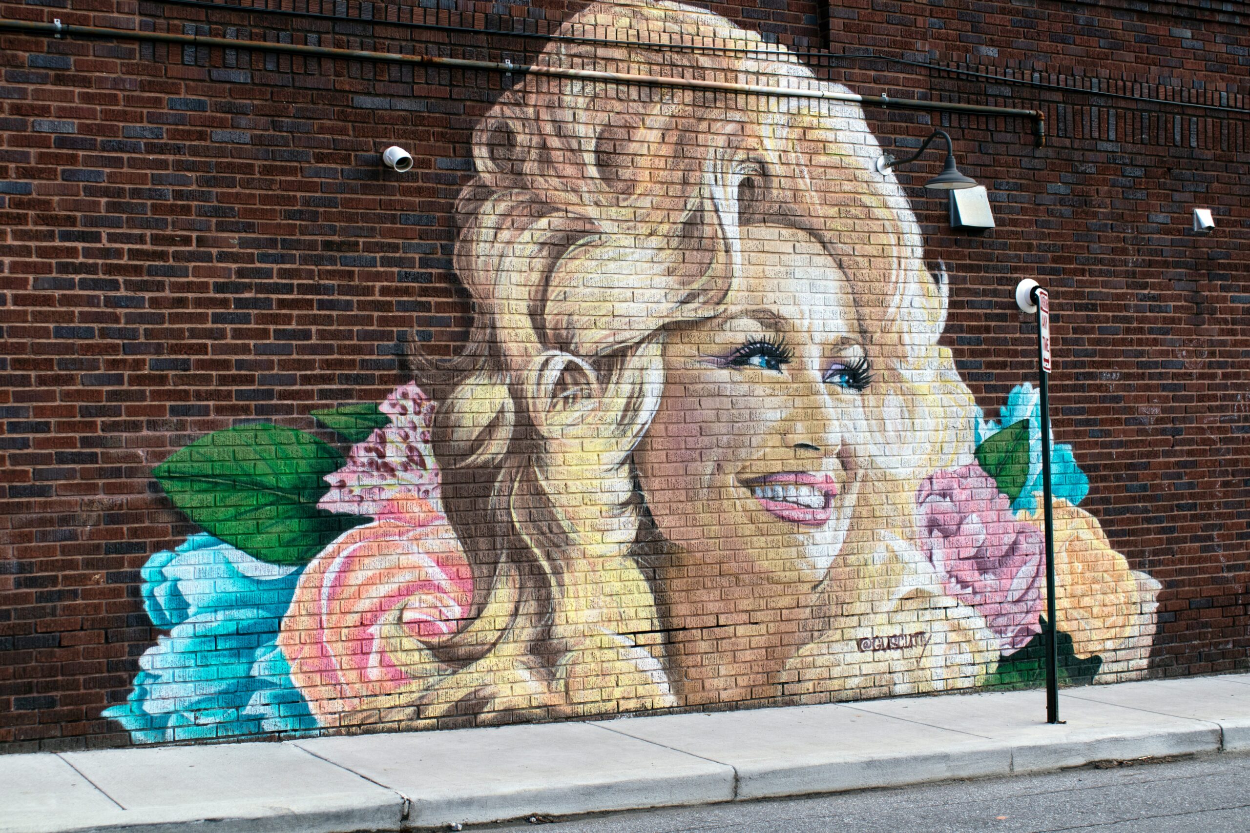 Photo of a mural of Dolly Parton on a brick wall.
